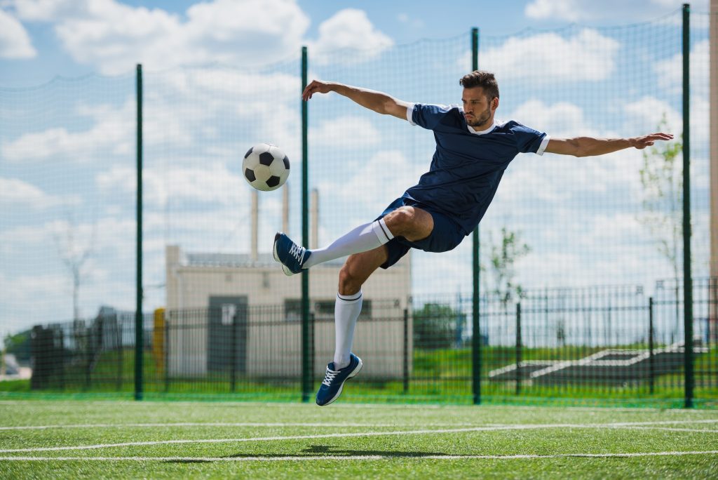 athletic soccer player kicking ball on soccer pitch